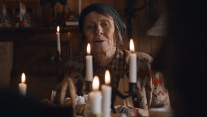 En hjälpande eller stjälpande hand? Kari Simonsen spelar en rollkaraktär som får en att associera till pepparkakshuset i Hans & Greta. En äldre dam sitter bakom en klunga levande ljus vid ett julbord.