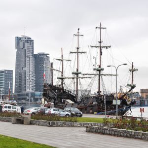 Det svarta piratskeppet Dragon ligger vid kajen i Gdynia, med gräsmatta och bilar framför och höghus i bakgrunden.