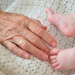 Vanhan naisen käsi koskettaa vauvan jalkoja.