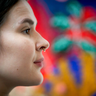 En ung kvinnas ansikte i profil mot bakgrund av en målning. 