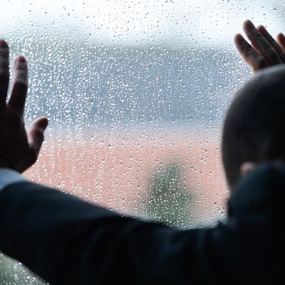 Mies nojaa sateen kastelemaan ikkunalasiin.