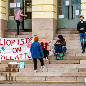 Banderolleja ja ihmisiä opiskelijoiden valtaaman Helsingin yliopiston päärakennuksen pääsisäänkäynnin edessä.