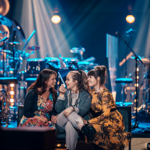 Kolme naista istuvat SuomiLOVEn lavan reunalla nauraen.