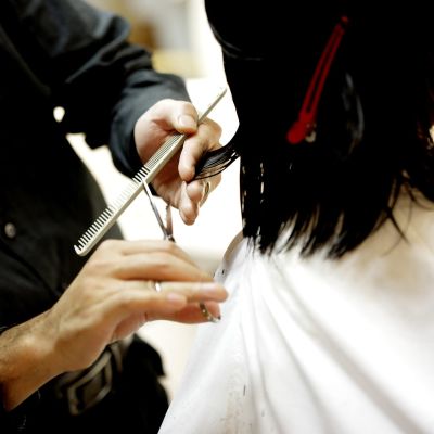En frisörs händer som klipper ett mörkt axellångt hår