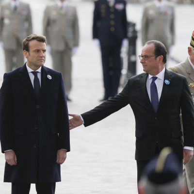Hollande ojentaa kättä varautuneelle Macronille, taustalla univormupukuisia veteraaneja.