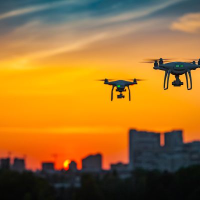 Kaksi dronea lentää iltaruskossa.