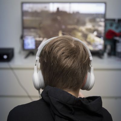 poika pelaa tietokonepeliä kuulokkeet päässä
