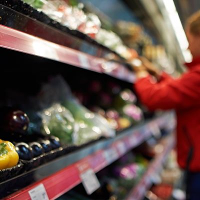 Työntekijä täyttää vihanneshyllyä supermarketissa.