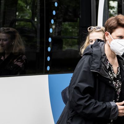 Nainen kasvomaskiin suojautuneena bussipysäkillä.