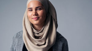 Iman Meskini föreläser om livet som ung muslim i Norge. Hon är van vid att svara på alla möjliga frågor och jobbar för att sprida kunskap och krossa förutfattade meningar om muslimer. Iman står mot en grå bakgrund med en beigefärgad hijab och en rutig kavaj.