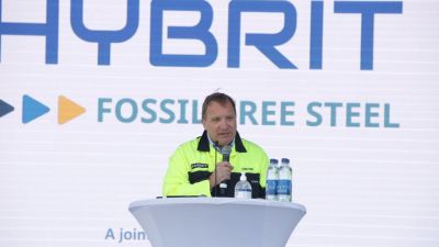 Stefan Löfven i industriskyddsjacka talar vid ett podium vid stålverket.