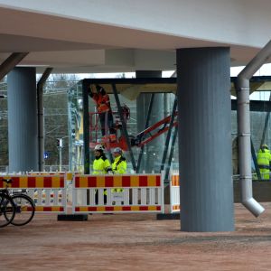 Nägra byggnadsarbetare arbetar vid en glasinhägnad under en bro.