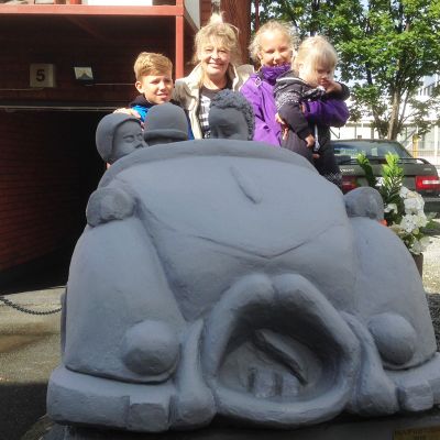 Päivi Kinnunen veistämässään Aku Ankka -betoniautossa lastenlastensa Konstan, Annikan ja Josefiinan kanssa.