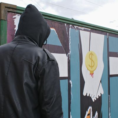 Mustaan huppariin pukeutunut mies seisoo julistemaisen katutaidetyön edessä.