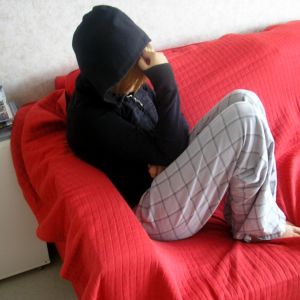 Ung person som döljer sitt ansikte i en huva sitter på soffan