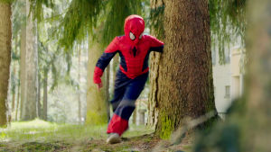 Lapsi Spiderman-puvussa juoksee metsässä.
