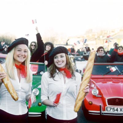 Baskeriin pukeutuneet naiset heiluttelevat patonkeja Citroen-autojen kokoontumisajoissa.