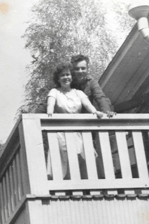 Erik tycker hans mamma ser så lycklig ut i sällskap av den okända mannen. En gammal svartvit bild av en kvinna och en man som står nära varandra på en balkong och tittar in i kameran.