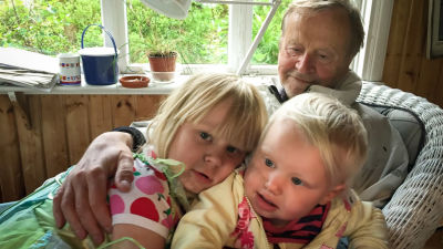 En äldre man sitter med två små barn i famnen.