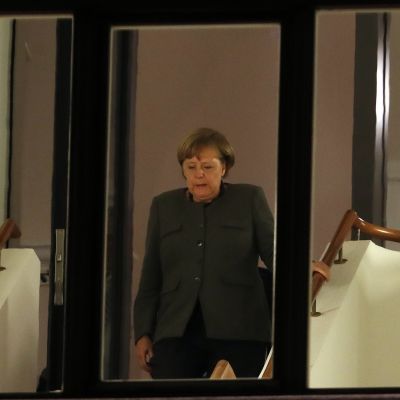 Angela Merkel portaissa kuvattuna ikkunan läpi.