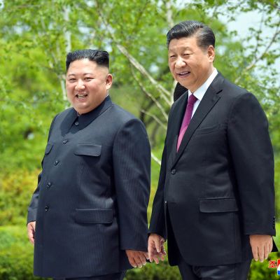 Kim Jong-un ja Xi Jinping kävelevät vihreässä puistomaisessa maisemassa.