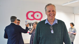 Jouni Malmivaara är ordförande för företagarföreningen i Lovisa. Han och hans kolleger har märkt att det kan vara svårt att haffa stadens kontrakt. Arkivbild. En man står i ett öppet utrymme och ler. Bakom hono syns andra personer som diskuterar.
