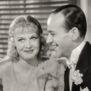Ginger Rogers hymyilee leuka mutrussa, vieressä häntä kohti leveästi hymyilevä Fred Astaire.