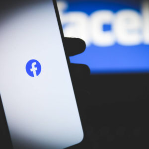 Facebookin logo kännykän ruudulla, kuvan taka-alalla sumeana teksti Facebook.