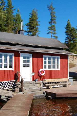 Punainen sauna valkoisilla ikkunankarmeilla seisoo vesistön ja laitureiden edessä.