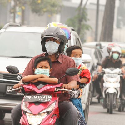 Hengityssuojaimilla varustautunut perhe ajamassa skootterilla Pekanbarussa, Indonesiassa.