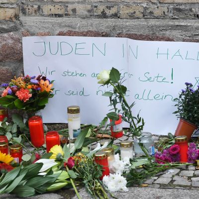 Maassa on kukkia ja kynttilöitä, sekä saksankielinen lappu, jossa lukee "Hallen juutalaiset, olemme rinnallanne, ette ole yksin"