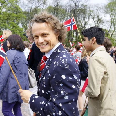 Nuori mies heiluttaa iloisesti Norjan lippua kulkueessa Norjan kansallispäivänä.