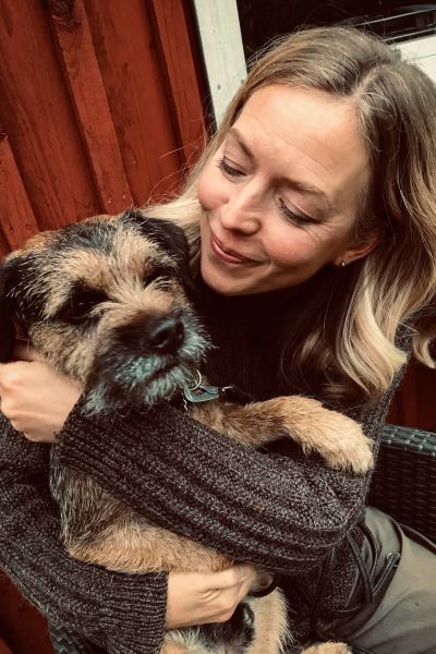 Linda Zilliacus sitter med ein hund i famnen. Båda ser väldigt nöjda ut.