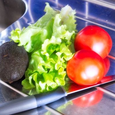 Avokado, salaaattia ja tomaatteja tiskipöydällä.