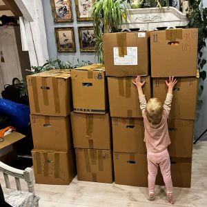 Ett barn på tv-tre år står med ryggen mot kameran och sträcker sig på tå för att försöka nå det stora "berget" av bruna papplådor. I lådorna finns kläder till barn i Ukraina.