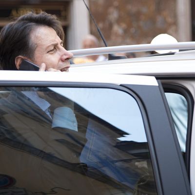 Kuvassa Giuseppe Conte on auton auki olevan oven takana puhumassa kännykkään.