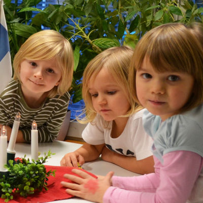 Fem barn sitter kring ett bord, i mitten på bordet en luciakrona.