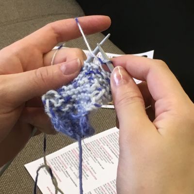 Naisen kädet neulomassa sinivalkoisesta langasta.