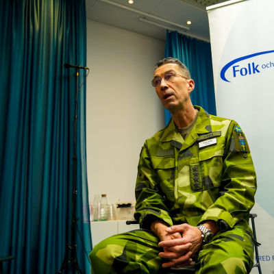Sveriges överbefälhavare Micael Bydén sitter vid en skylt där det står Folk och Försvar.