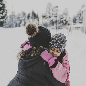 ett barn kramar om en vuxen ute på en snöig gård.