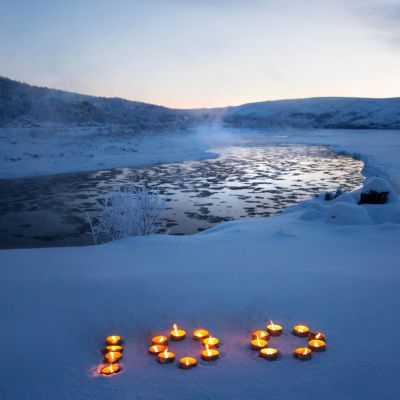 Talvinen jokimaisema, jossa kynttilöistä tehty numero 100.