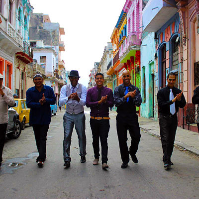 Sju män går i bredd på en gata i Havanna.