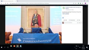 Professor Xinning Song föreläser på Konfuciusinstitutet vid Helsingfors universitet år 2016. Bilden är från Konfuciusinstitutets egen facebook-sida Xinning Song ser på en skärm som är draperad i blått tyg, bakom syns ett porträtt på universitetet