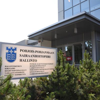 Pohjois-Pohjanmaan sairaanhoitopiiri hallintorakennus, jonka ulko-oven edessä opastekyltti.