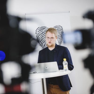 Rasmus Aro fotad på presskonferens när han talar vid podium