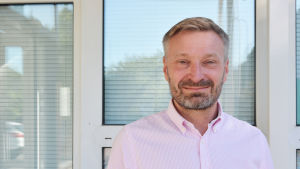 Tf servicechef Krister Lindman. En medelålders man i rosa kragskjorta står utomhus framför ett hus.