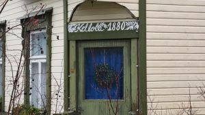 På Kellola välkomnar man julen. En ingång till ett ljusgult trähus med gröna kanter. Ovanför dörren står det Kellola 1880.