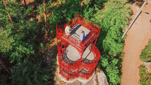 Ylhäältä kuvattu punainen näköalatorni kalliolla, tornissa kaksi ihmistä.
