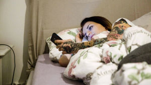 Om man mår dåligt blir ofta sömnen lidande och då blir det svårt att orka med jobbet. En ung kvinna ligger i sängen och tittar på sin mobiltelefon.