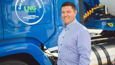 Man i blårutig skjorta står framför gasdriven långtradare.